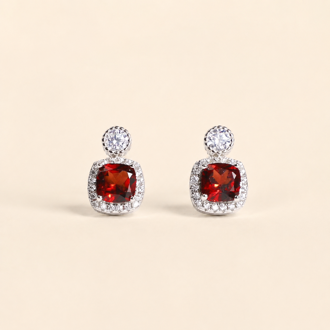 Natural garnet halo stud earrings on a warm ivory background